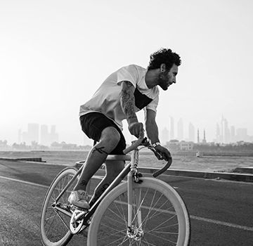 a black and white photo of a male riding a bicycle on the road next to the water